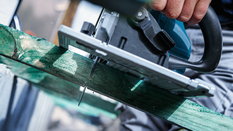 Person using a circular saw to cut a green wooden plank.