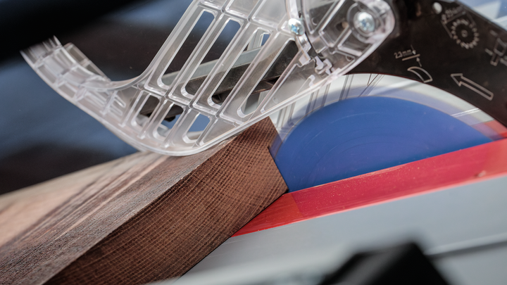 Object #200585336: 7557712_app_web_01 Circular saw cutting through a piece of wood under a transparent blade guard.