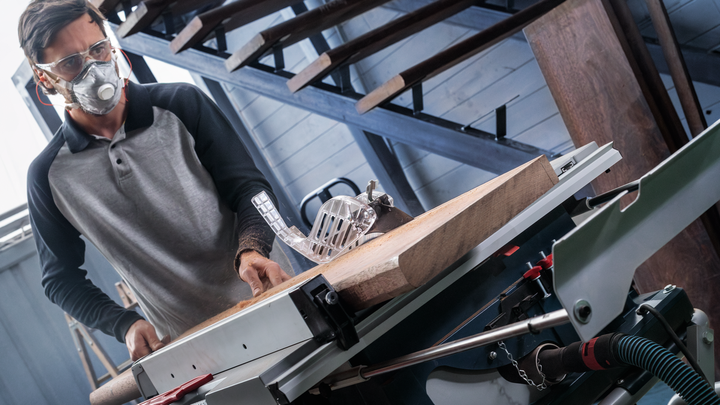 Object #200585344: 7557712_app_web_09 Person wearing safety equipment cuts wood on a table saw.