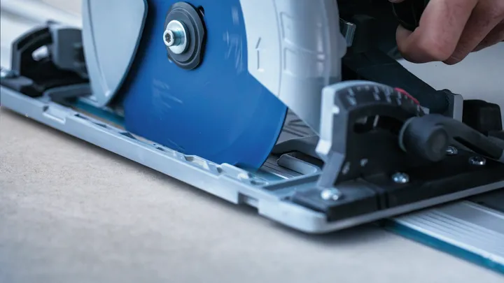 Object #200585529: 7557691_app_web_06 Person guides a circular saw along a metal track to cut a sheet of wood.