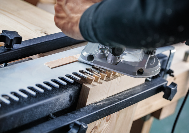 Person guides a router to cut precise joints in a wooden board.