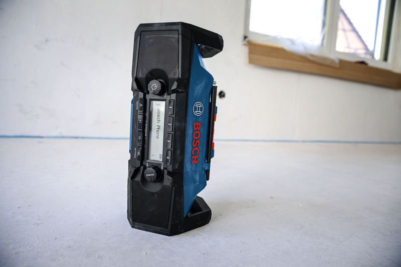 Portable jobsite radio standing on a concrete floor in a room under renovation.
