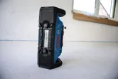 Portable jobsite radio standing on a concrete floor in a room under renovation.