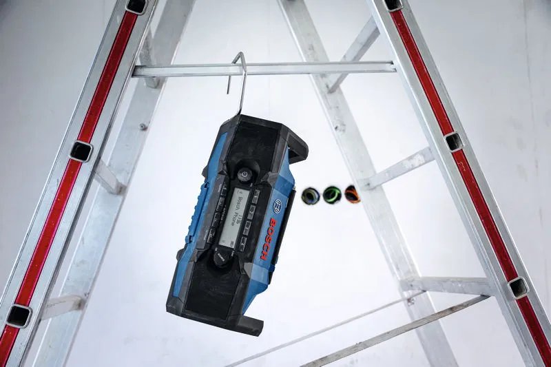 Jobsite radio hanging from a metal rod between two ladders.