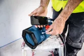 A person wearing safety equipment charges a smartphone using a portable jobsite radio.