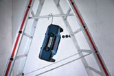 Job site radio hanging from a metal hook on a ladder in a construction area.