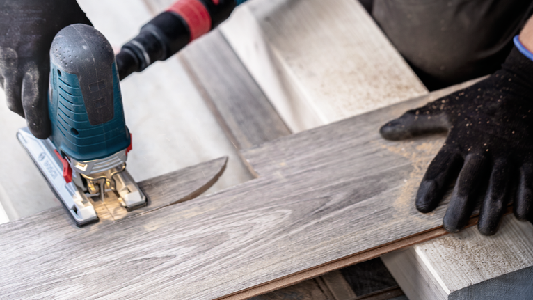 Person wearing safety equipment cuts laminate flooring with a jigsaw.