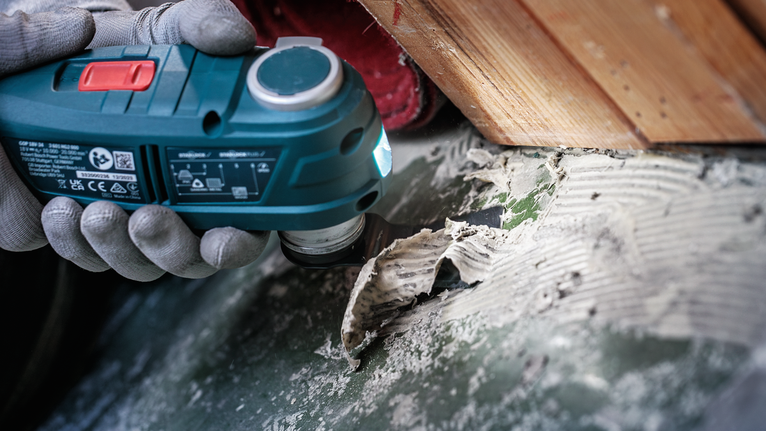 Person wearing safety equipment uses a power tool to remove adhesive from a hard surface.