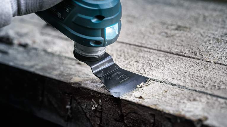 Person using a power tool with a scraper blade to remove material from a wooden surface.