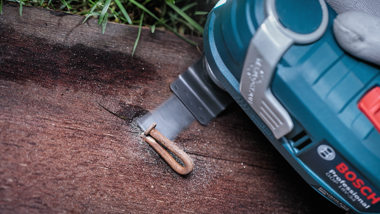 Oscillating tool cutting a metal staple embedded in a wooden board.