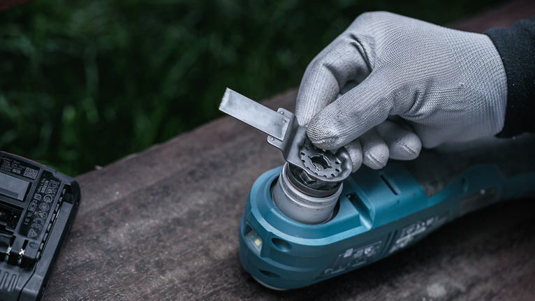 Person wearing safety equipment attaches a metal blade to a power tool.