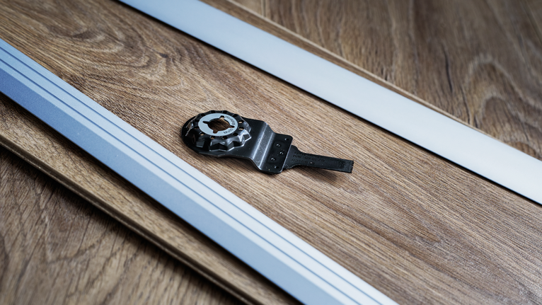 Oscillating tool blade and guide rails placed on a wooden floor surface.