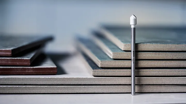 Diamond tile drill bit standing upright in front of stacked ceramic tiles.