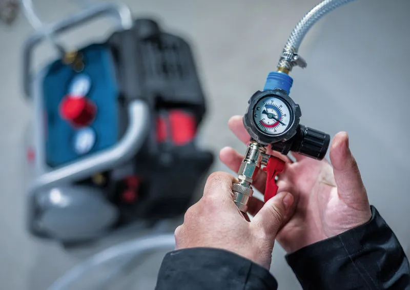 A person adjusts a pressure gauge attached to an air compressor.