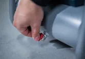 A person turns a red valve on a gray cylindrical machine.