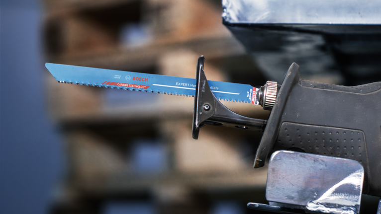 Reciprocating saw with a blue blade cutting through a metal pipe.