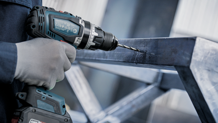 Person wearing safety equipment drills into a steel beam.