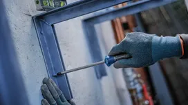 Person wearing safety equipment uses a screwdriver to fasten a metal frame.