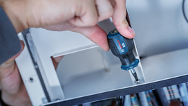 Person using a screwdriver to tighten a screw inside a metal enclosure.