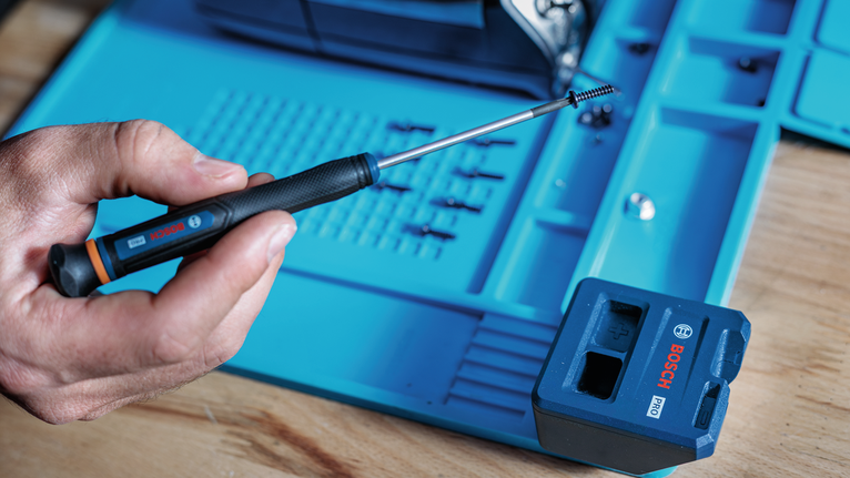 Person uses a screwdriver to hold a screw near a blue storage case on a wooden surface.