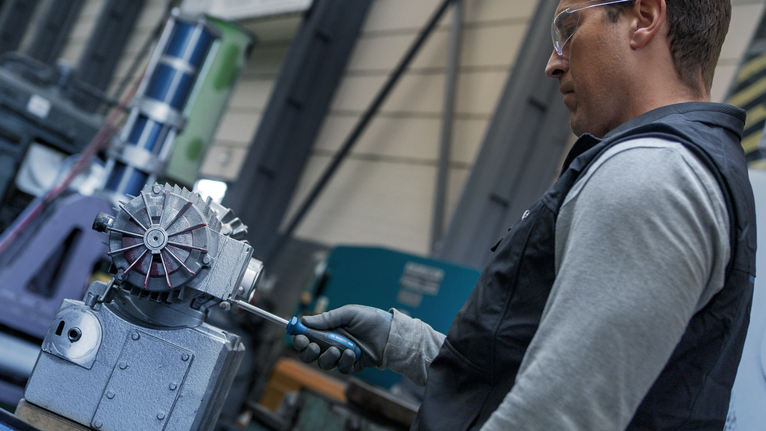 Person wearing safety equipment tightens a bolt on industrial machinery.