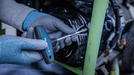 Person wearing safety equipment uses a screwdriver to tighten a screw on machinery.