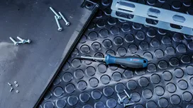 Screwdriver and various screws lying on a textured rubber mat.