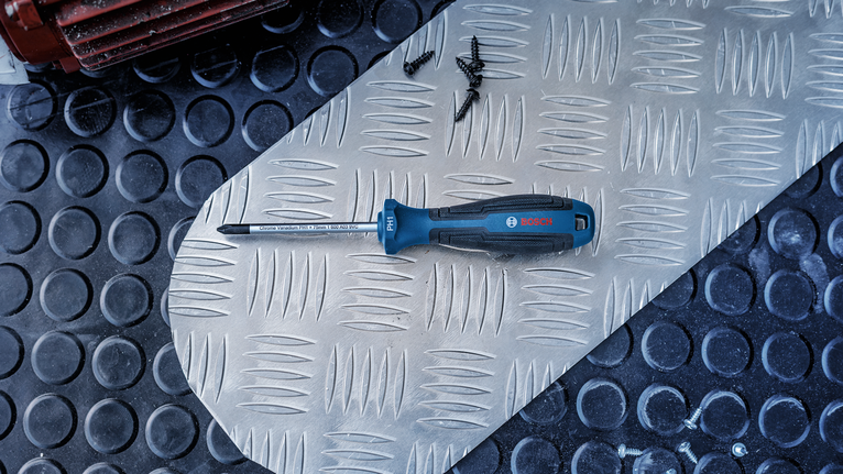 Phillips screwdriver and scattered screws lie on a metal tread plate.