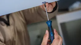 Person fastens a screw into the ceiling using a blue and black screwdriver.