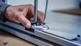 Person uses a screwdriver to adjust a metal fixture on a flat surface.