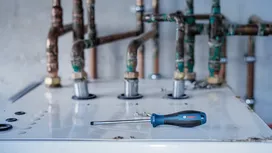 Flathead screwdriver lies on top of a boiler near several rusted pipes.