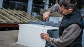 Person assembling a cabinet with a screwdriver in a workshop.