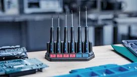 Set of precision screwdrivers in a charging dock on a workbench.