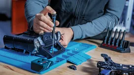 Person assembles a device on a blue workstation using a screwdriver.