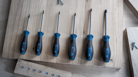 Six blue and black screwdrivers arranged by size on a light wood workbench.