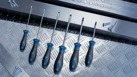 A set of screwdrivers arranged on a metal surface next to scattered screws.