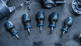 Five screwdrivers arranged on a metal workbench beside various machine parts.