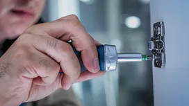 Person using a power screwdriver to install a hinge on a cabinet door.