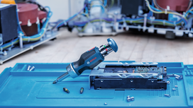 Cordless screwdriver with interchangeable bits lies next to an opened electronic device.