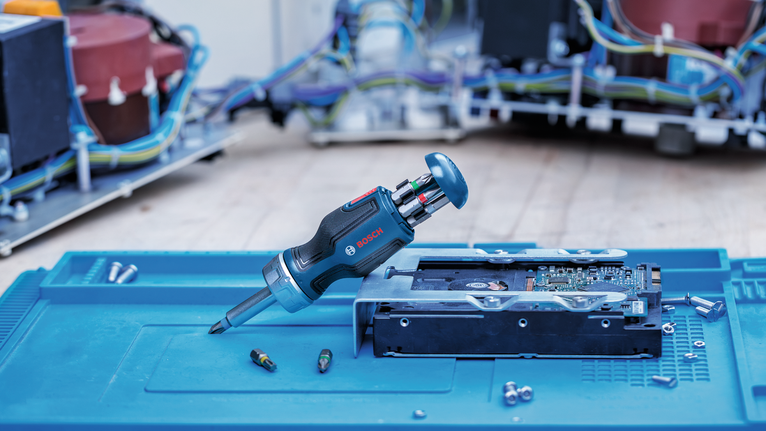 Cordless screwdriver with interchangeable bits lies next to an opened electronic device.