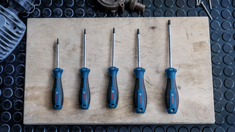 Five screwdrivers with blue and black handles arranged on a wooden board.