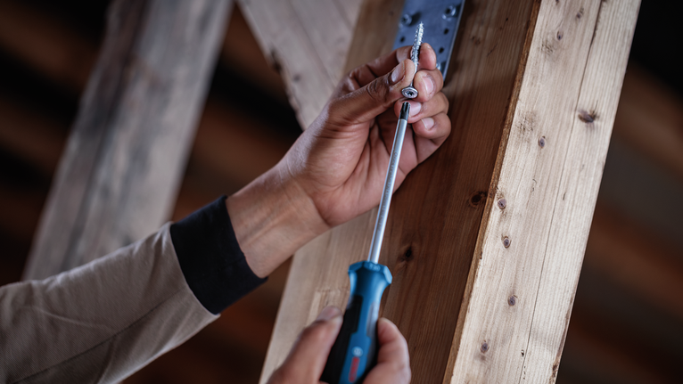 Person using a screwdriver to fasten a screw into a wooden frame.