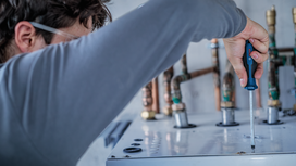 Person wearing safety equipment uses a screwdriver on a metal machine panel.