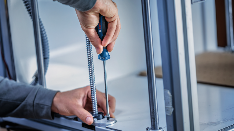 Person using a screwdriver to fasten a conduit into a metal base.