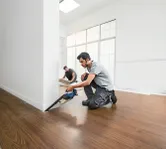 يقوم شخص ما بقطع الأرضيات بالقرب من الحائط باستخدام منشار لاسلكي بينما يقوم شخص آخر بتثبيت ألواح الأرضية.
