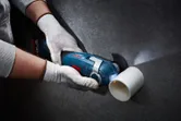 يقوم شخص يرتدي معدات السلامة بقطع أنبوب بلاستيكي أبيض باستخدام قاطع متعدد لاسلكي.