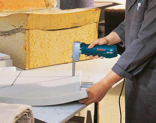 Person in work clothes trims foam material with an electric saw.