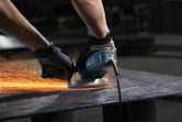 A person wearing safety equipment grinds metal, producing bright sparks.