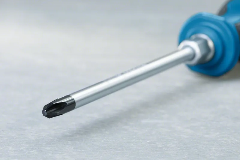 Phillips screwdriver with a blue handle lying on a gray surface.