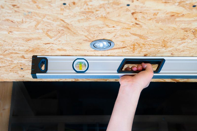 Person holding an optical level tool against a wooden ceiling.